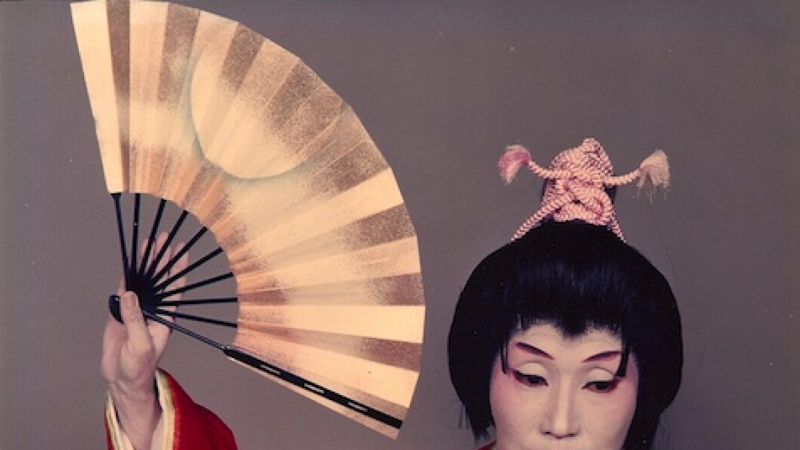 A female Japanese classical dancer in white face paint, a dark updo wig, holding a fan