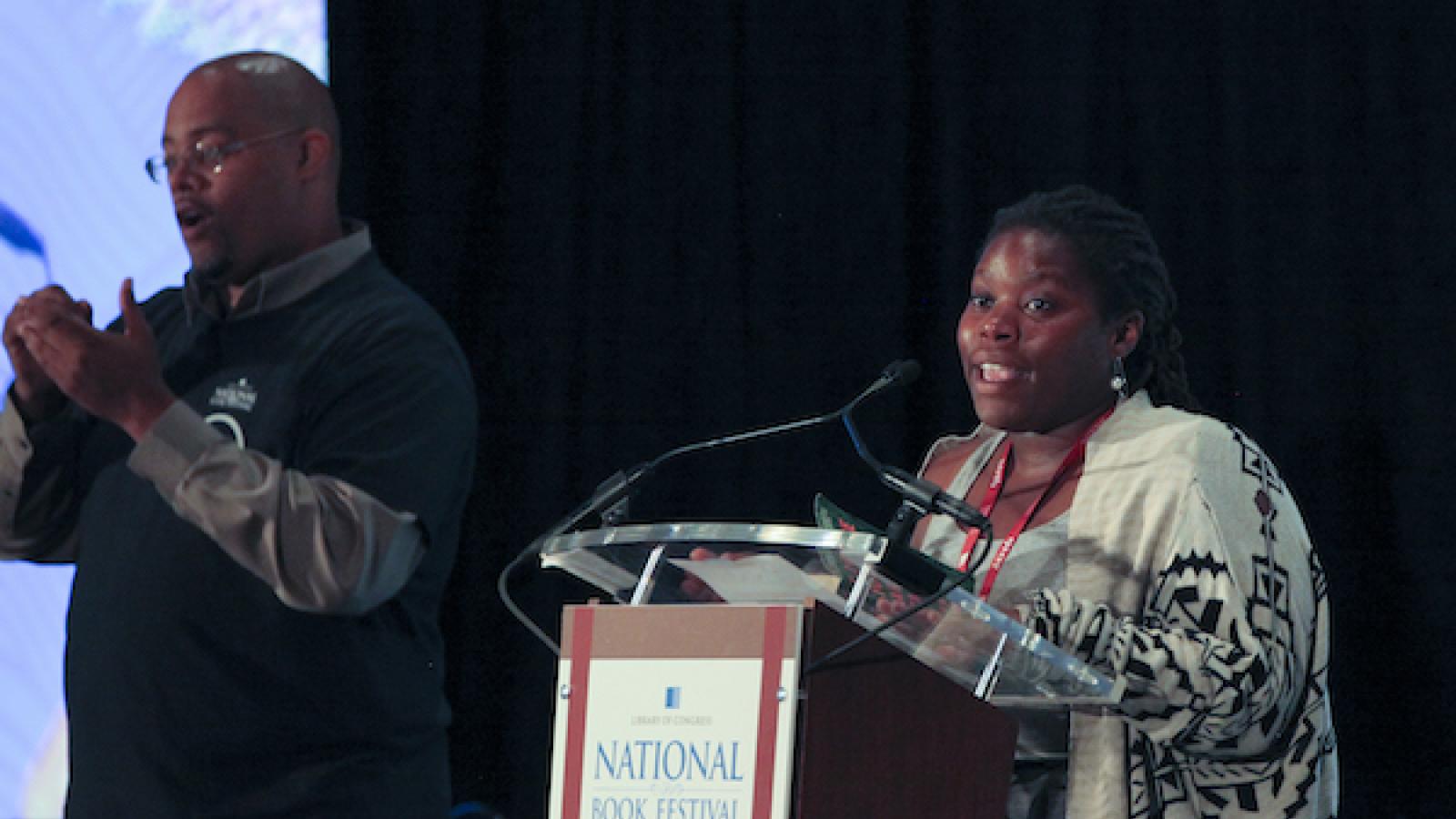 a young African American woman behind a podium with a sign language interpreter to her left