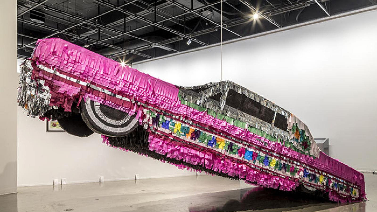Life-size lowrider car piñata hanging in a museum