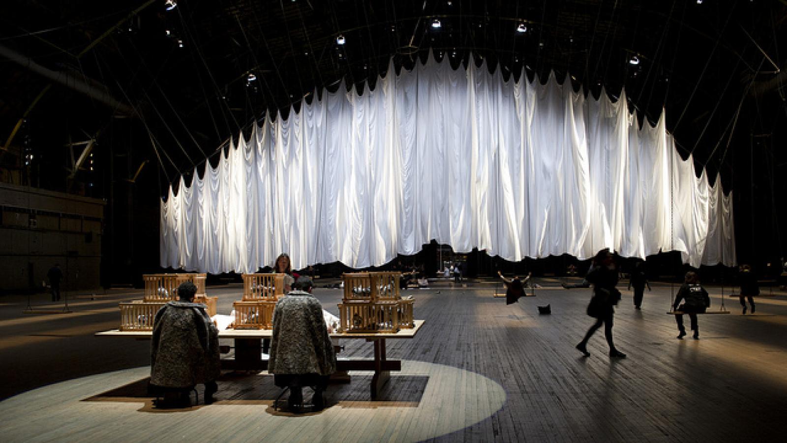 Ann Hamilton's installation the event of a thread Big billowy sheets hanging from ceiling in front of table with crates on it