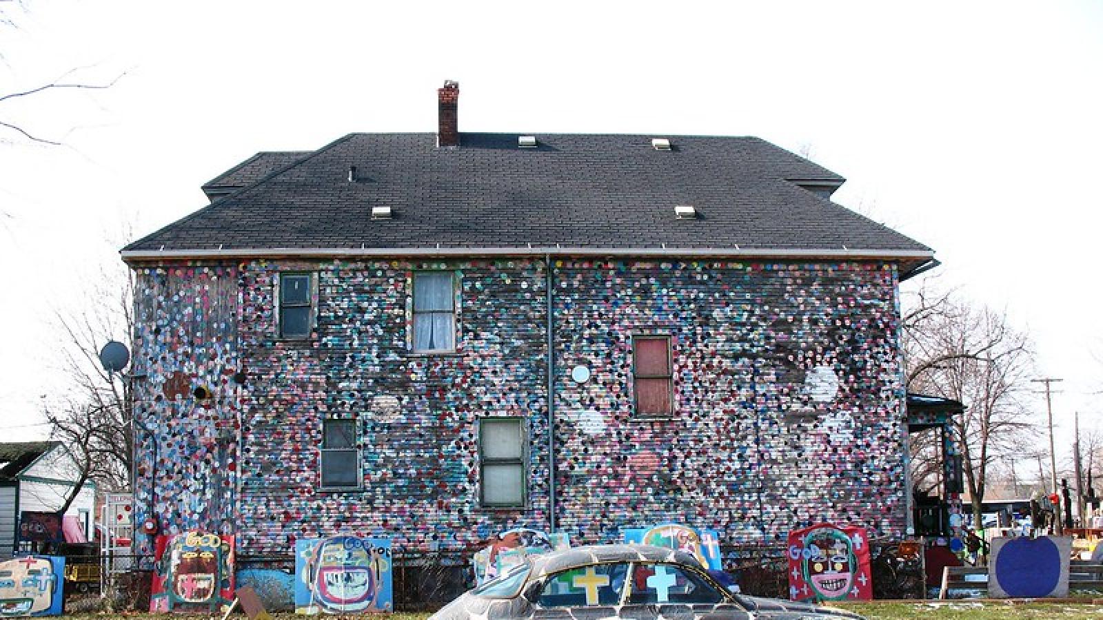 A house covered with colorful polka dots with colorful sculptures made from trash in the front yard