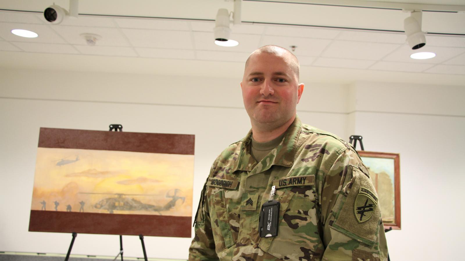 On left, painting of a grounded helicopter against an orange sky, to the right, a man in camouflage.