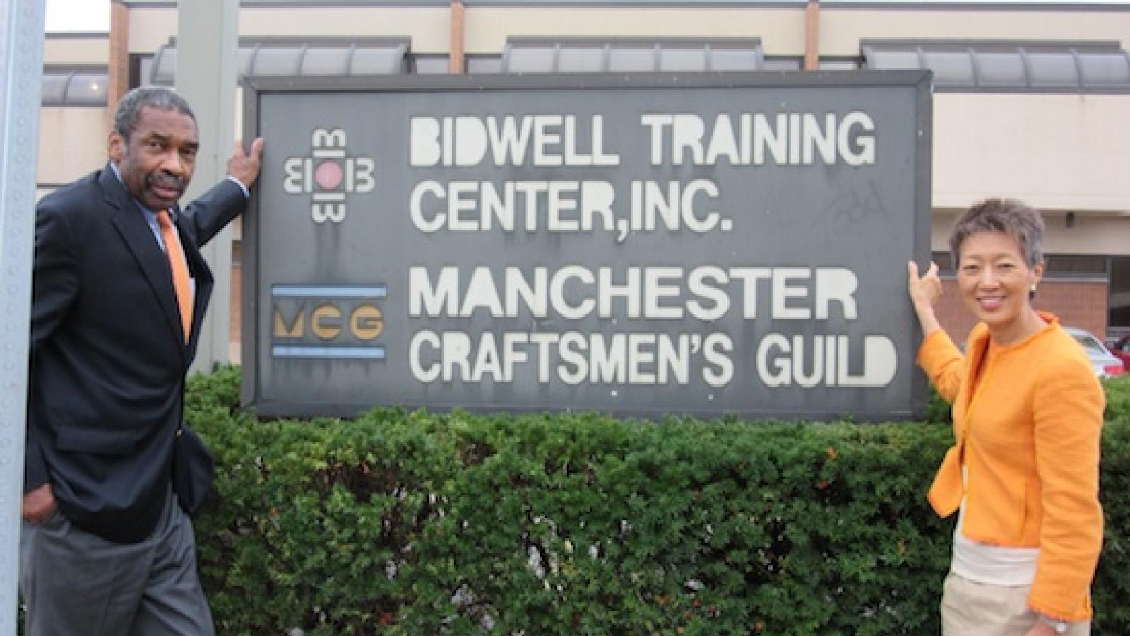 The Manchester Craftsmen Guild has a nationally recognized jazz program and has previously received NEA grant support. Bill Strickland and Jane Chu pose on either side of a vintage looking sign that reads Manchester Craftsmen's Guild