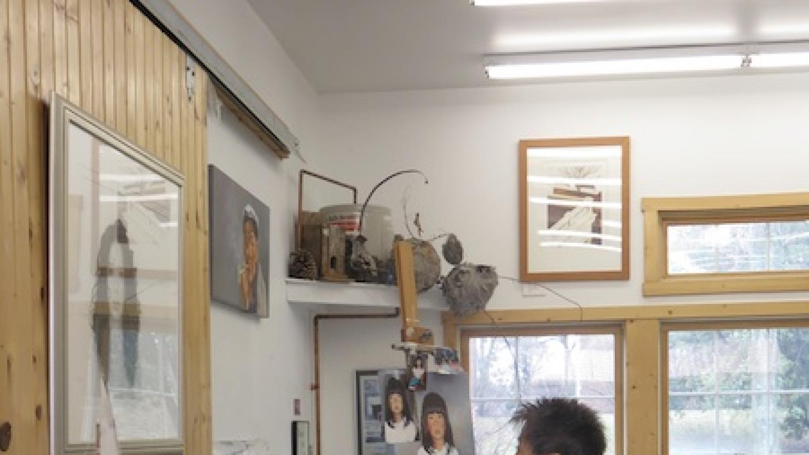 an Asian woman looking at art on paper in an art-filled studio space