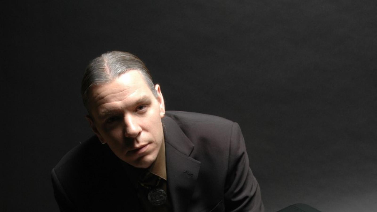 Jerod Impichchaachaaha' Tate Man in dark suit sitting on weight bench with sheet music scattered on ground