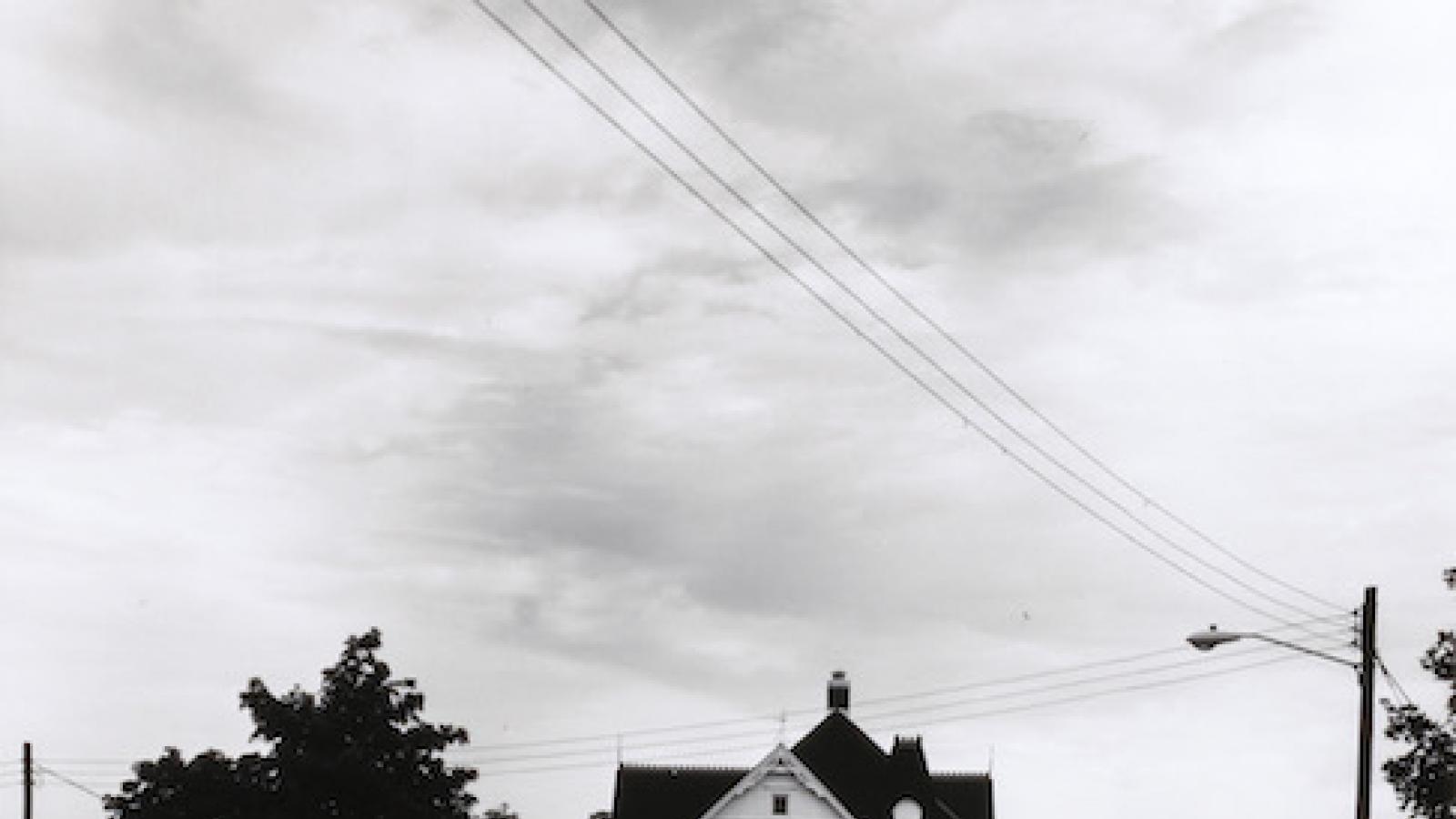 a two-story white wooden house seen at a distance down a road