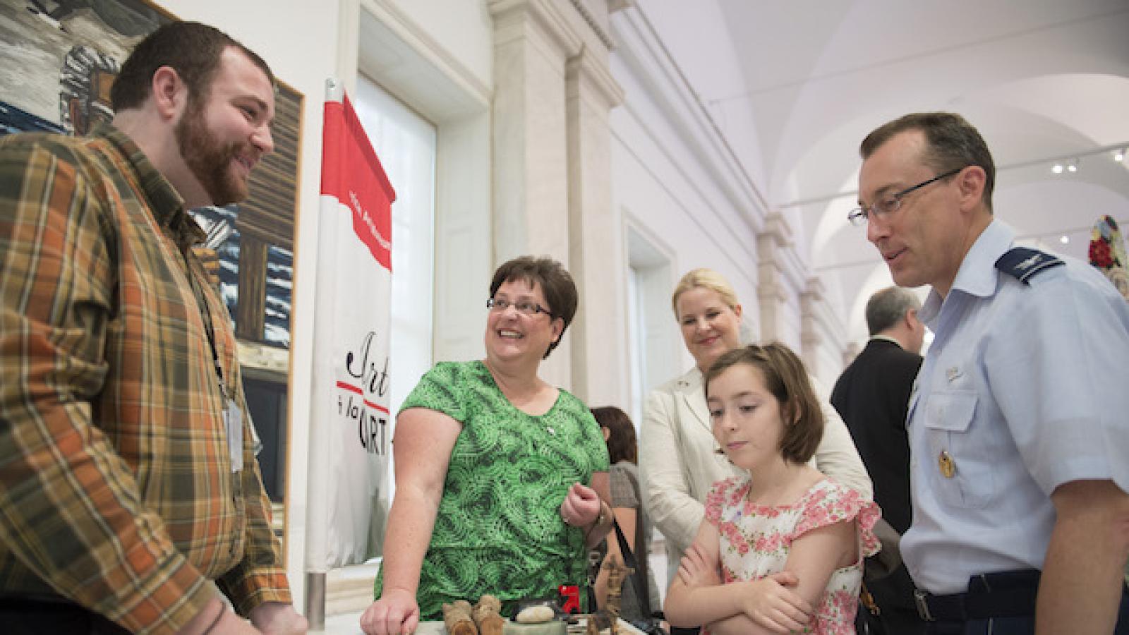 a family including a man in uniform watching a demonstration at an art museum