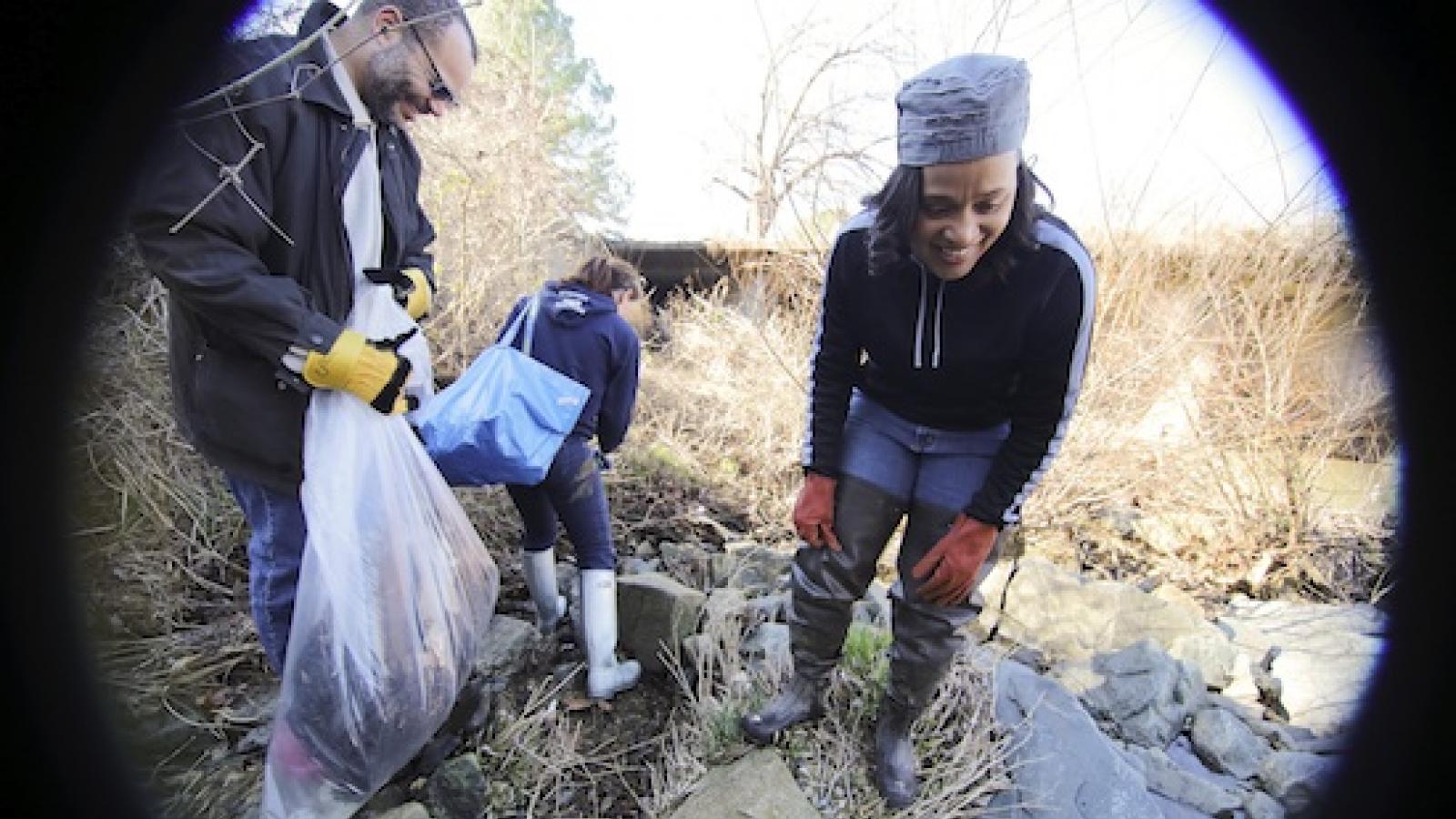Lisa Hoffman with two other people loading trash into bags alongside shallow waterway