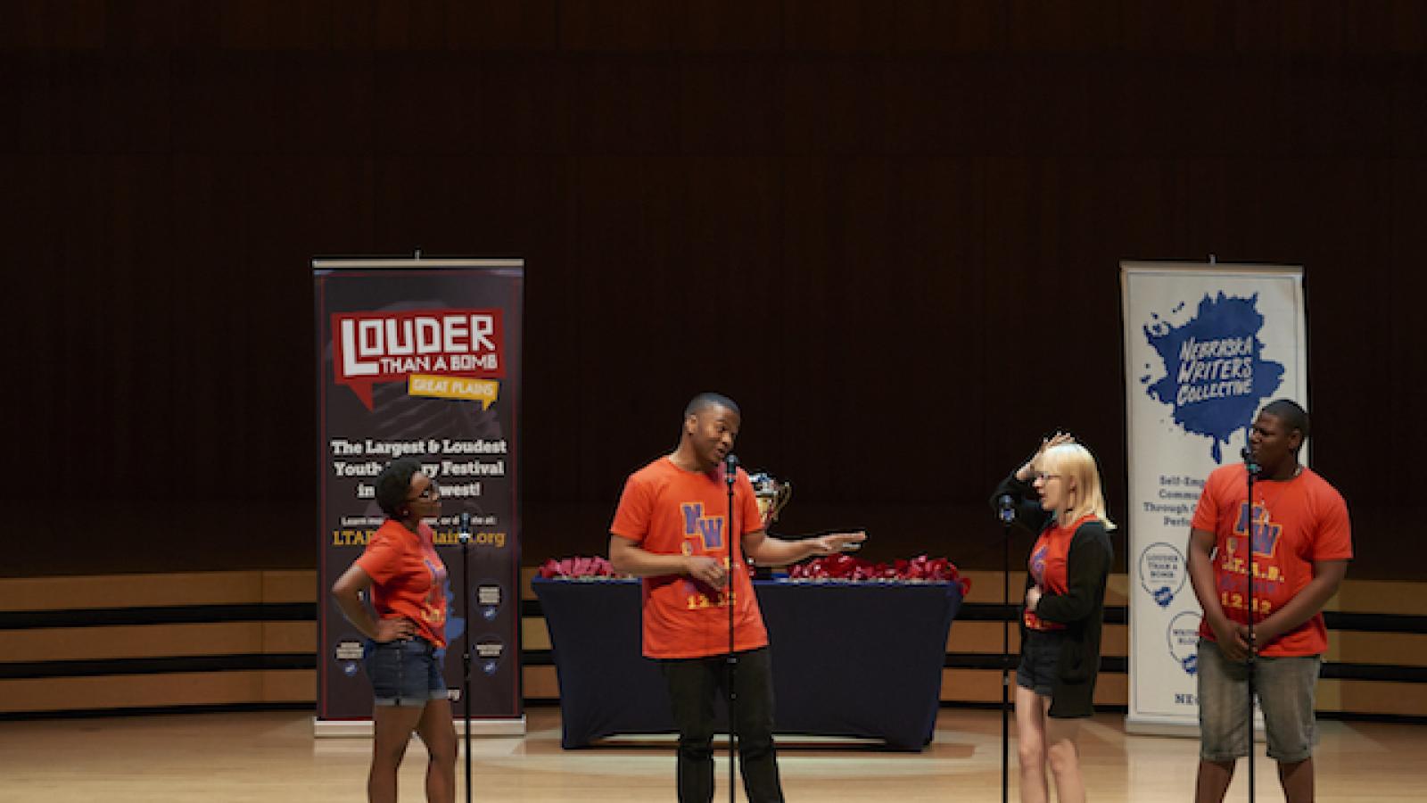 a group of four students on a stage with festival banners behind them