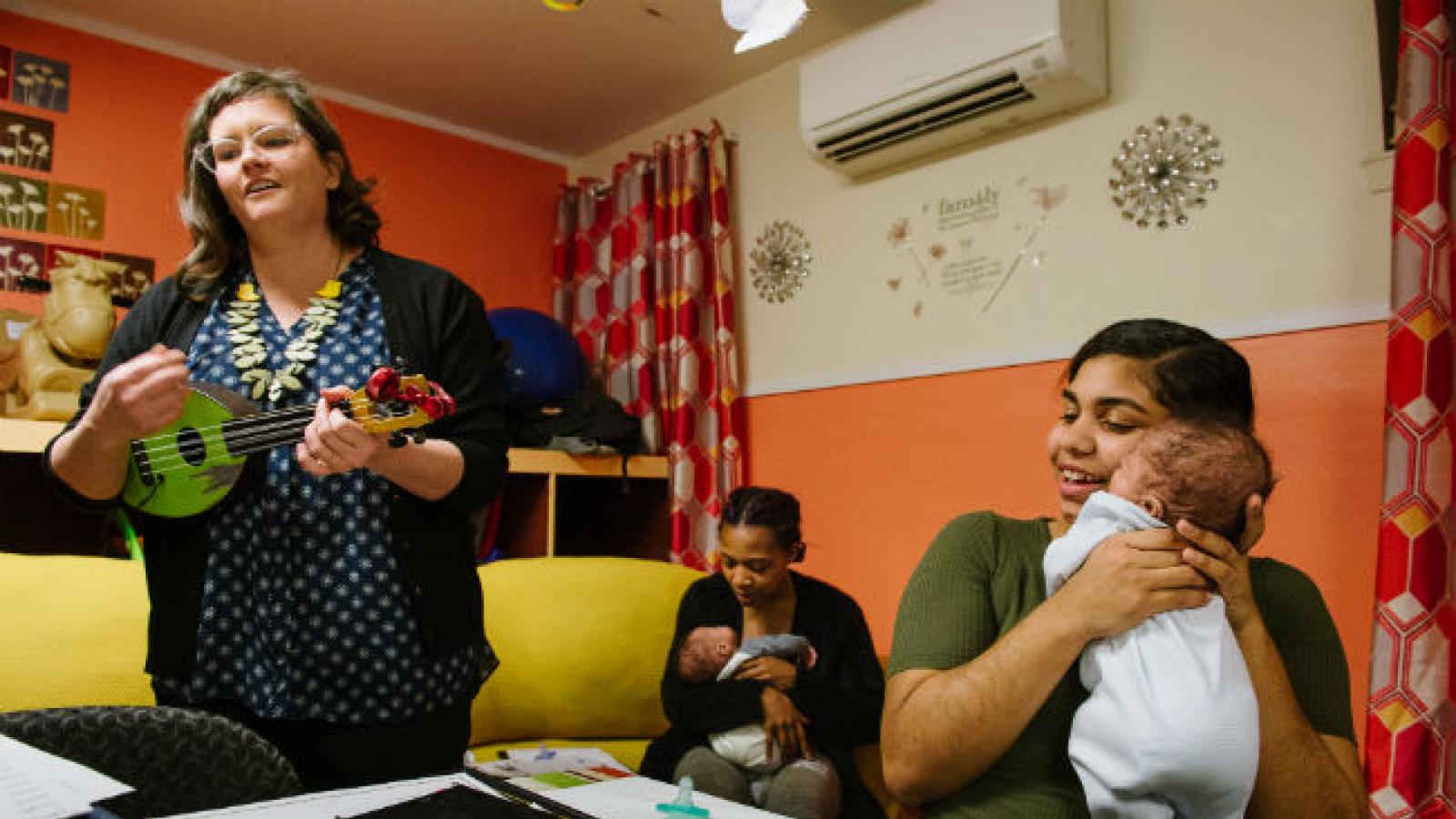 Women sharing lullabies they composed for their babies Women playing guitar next to woman holding baby