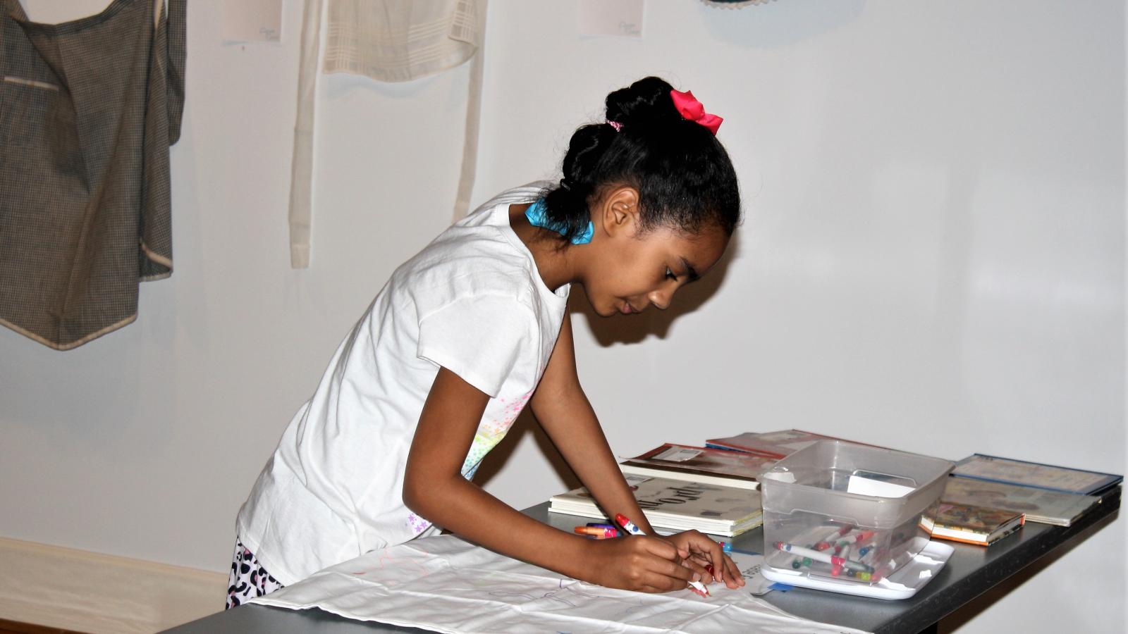 A young girl bends over and decorates an apron as part of an exhibition