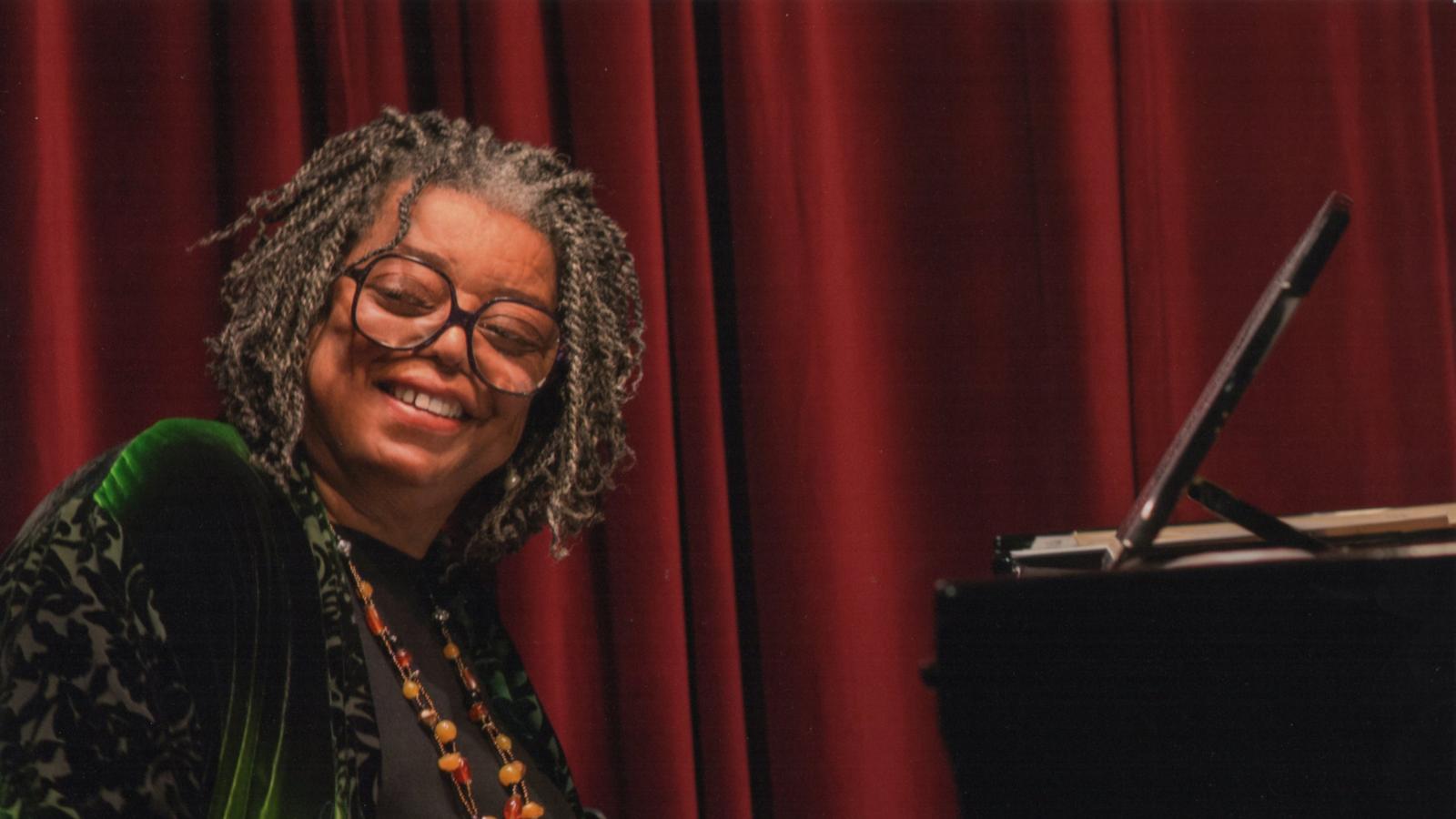 Mary Watkins smiling and sitting in front of a piano.