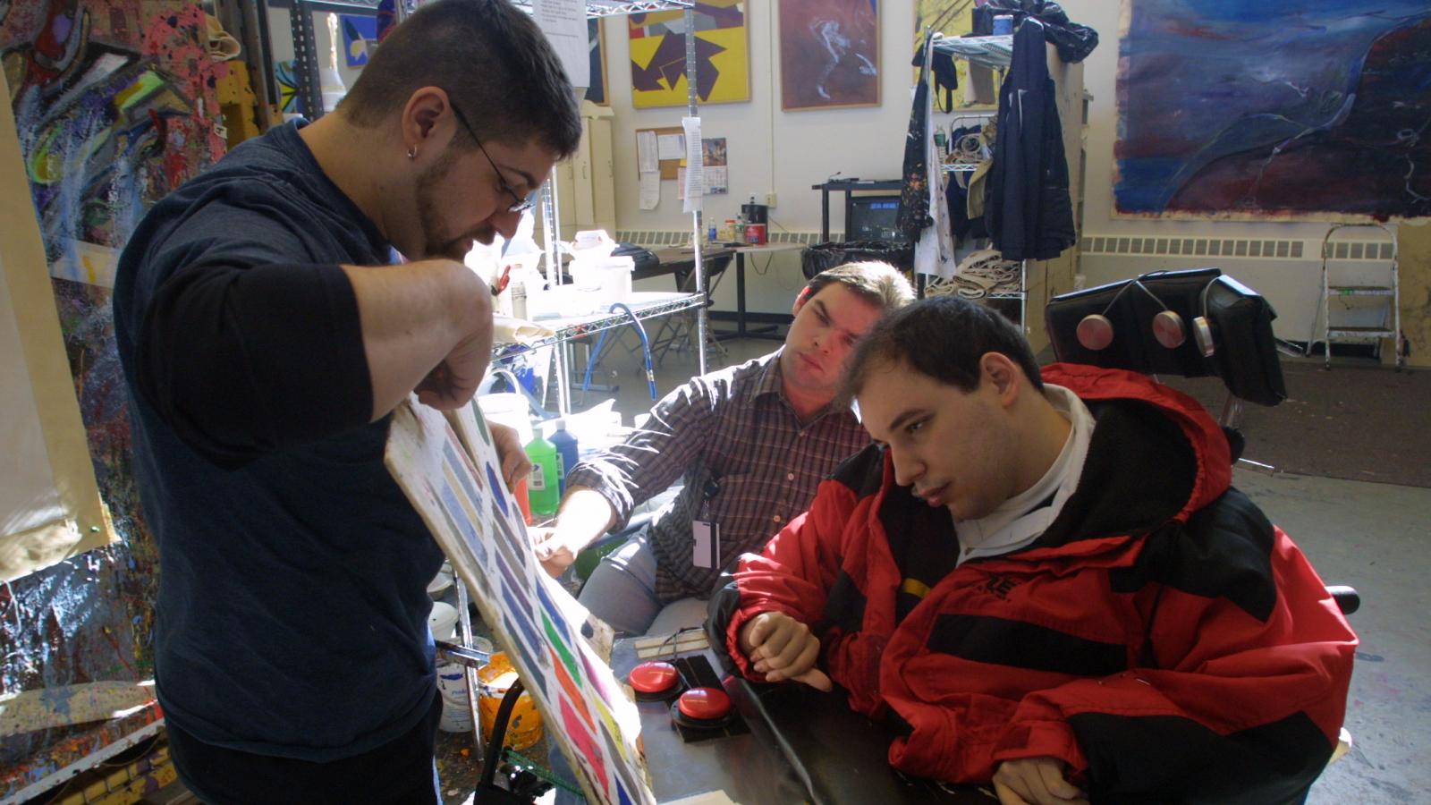 Man pointing to colors for man in wheelchair to choose. 