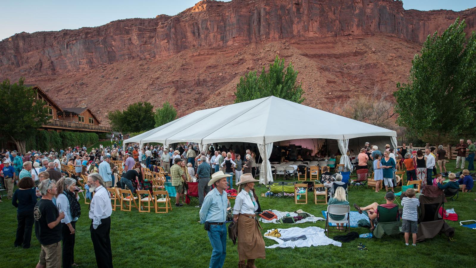 Festival attendees walking around with red rocks in the background and white tents posted up. 