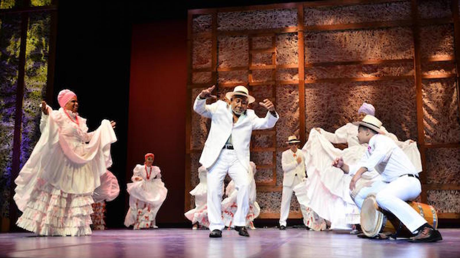 Heritage Fellow Modesto Cepeda on stage with male and female dancers in traditional white Puerto Rican costumes