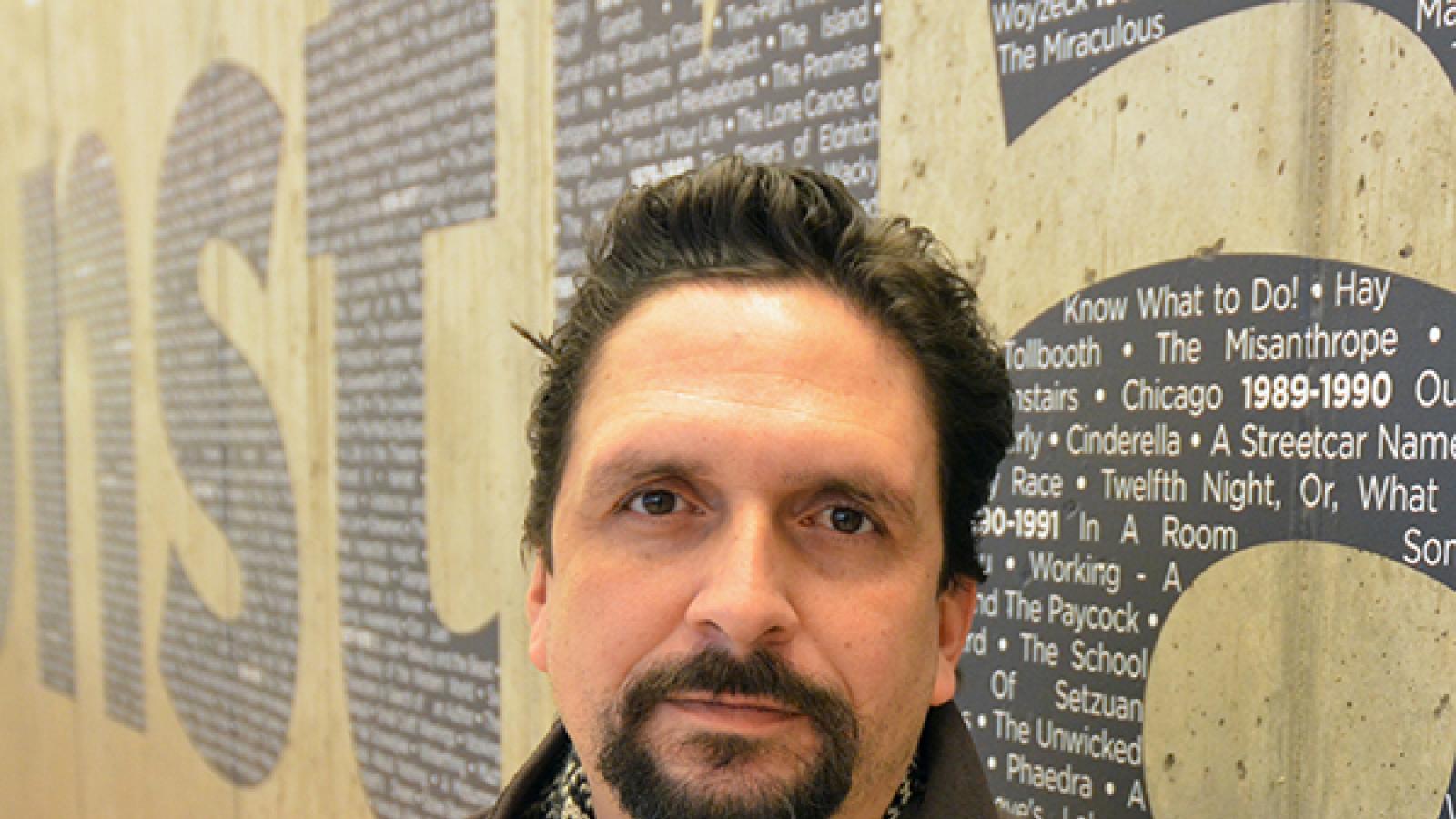 Man standing in front of wall with names of play written on it. 