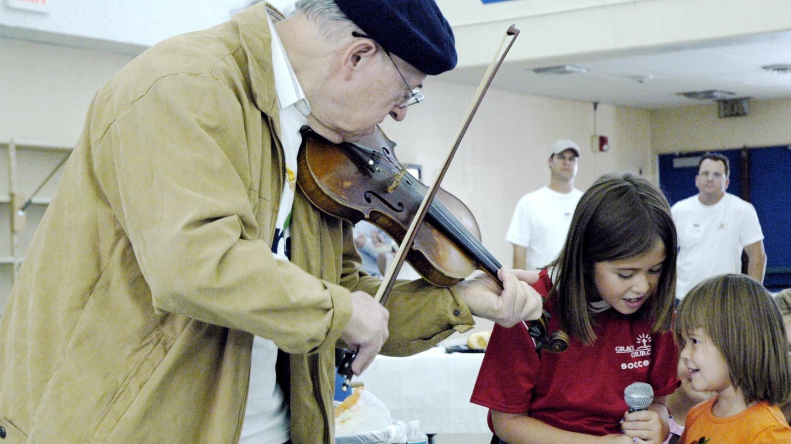 An elderly man playing violin to a couple of children.