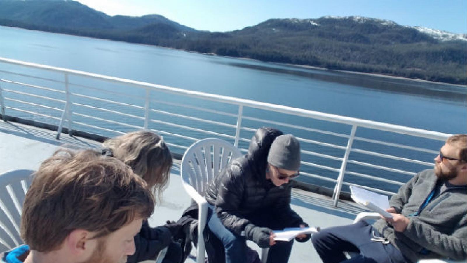 Tidelines Journey participants People reading papers sitting on the deck of a ferry in Alaska