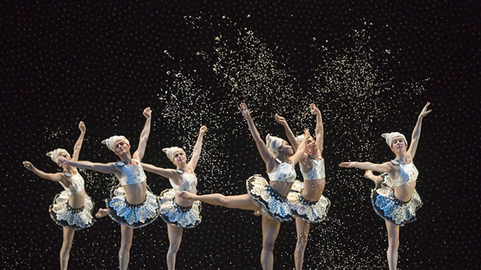 Dancers in tutus with arms in the air, dancing.