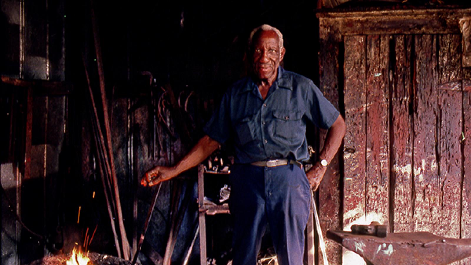 Man standing next to a fire for blacksmithing. 