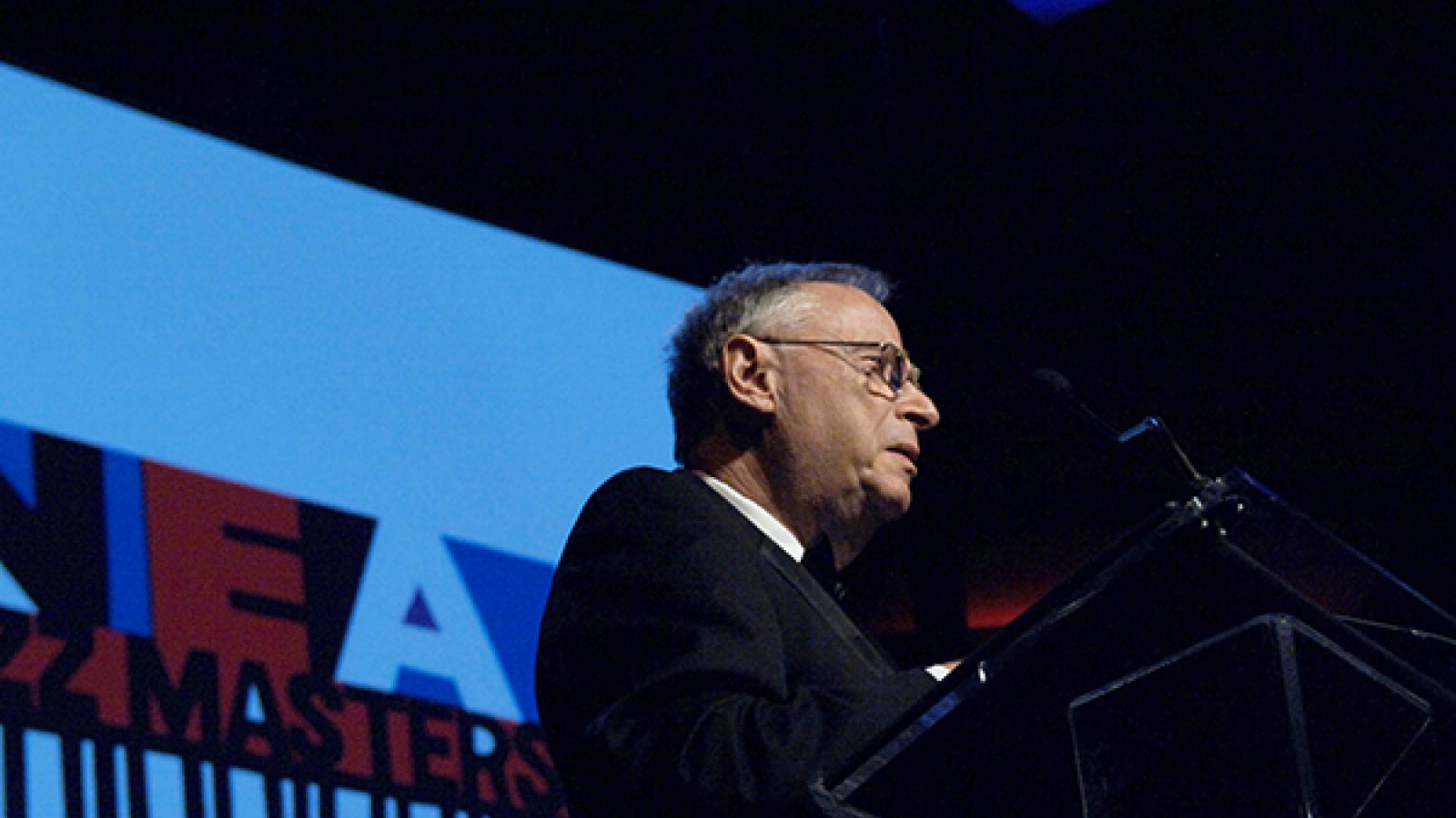 Man on stage in front of podium. 