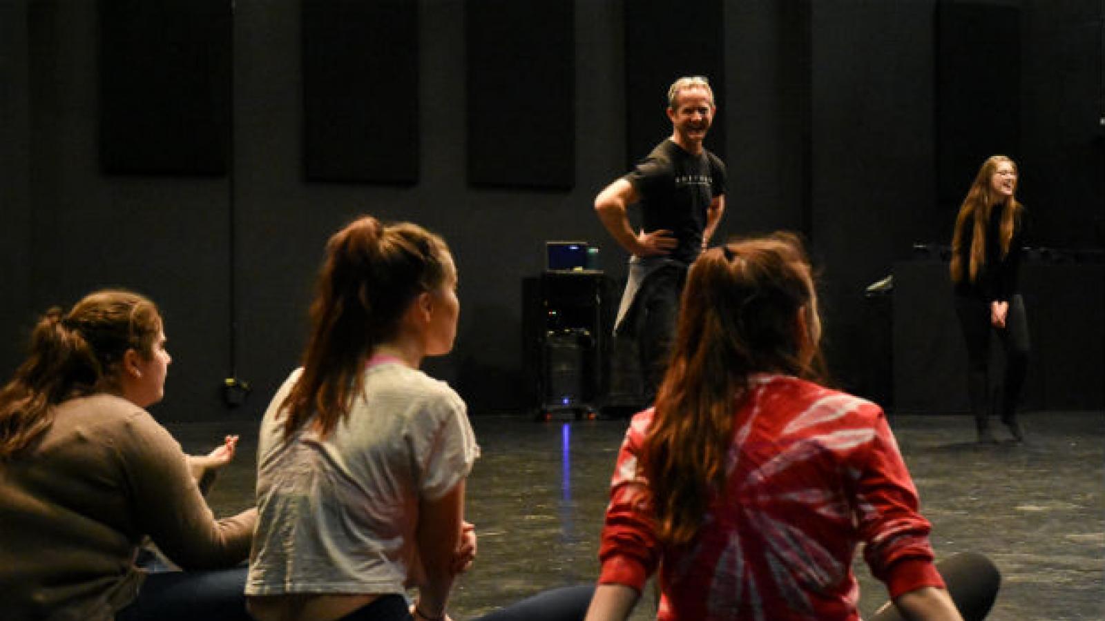 A dance workshop at Avanti High School A laughing man stands in a circle of seated high school students