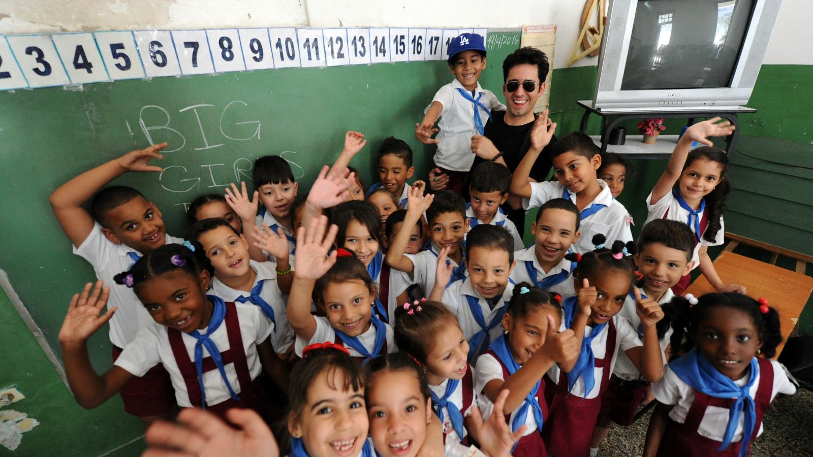 Dark-haired man stands with waving school children