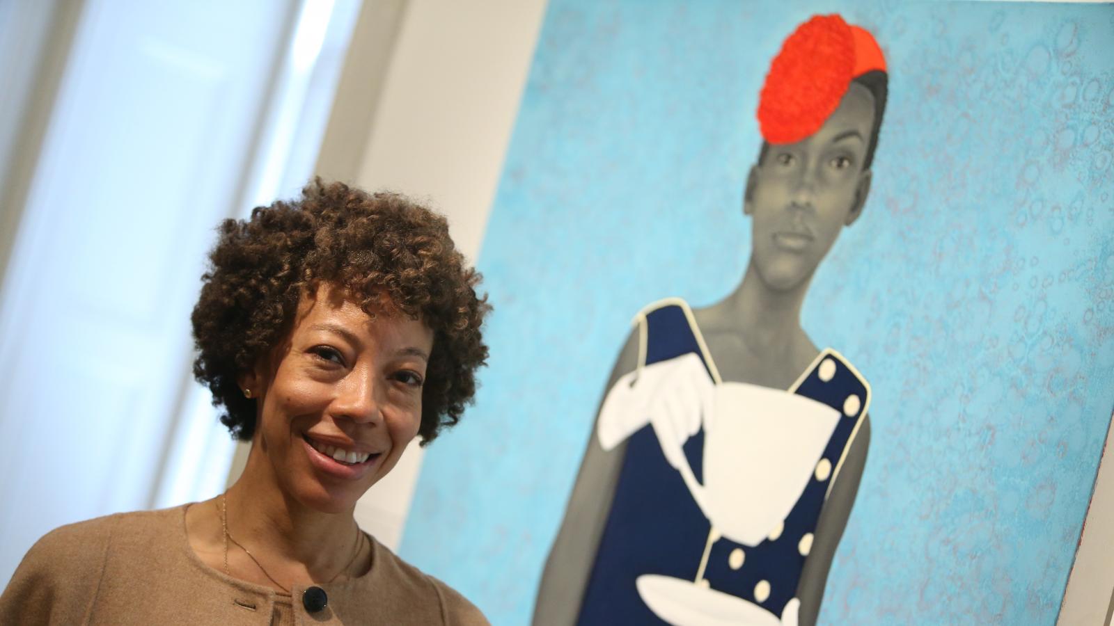 Artist Amy Sherald standing in front of her painting. 