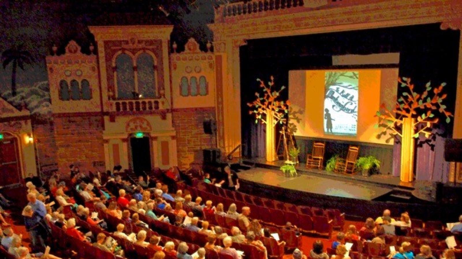 Bird's eye view of the inside of a theater. Stage decorated and room filled with people.