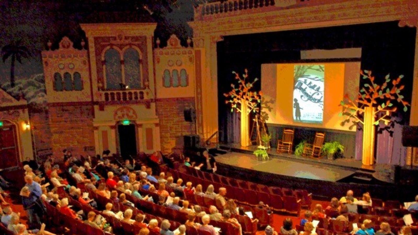 Bird's eye view of the inside of a theater. Stage decorated and room filled with people. 