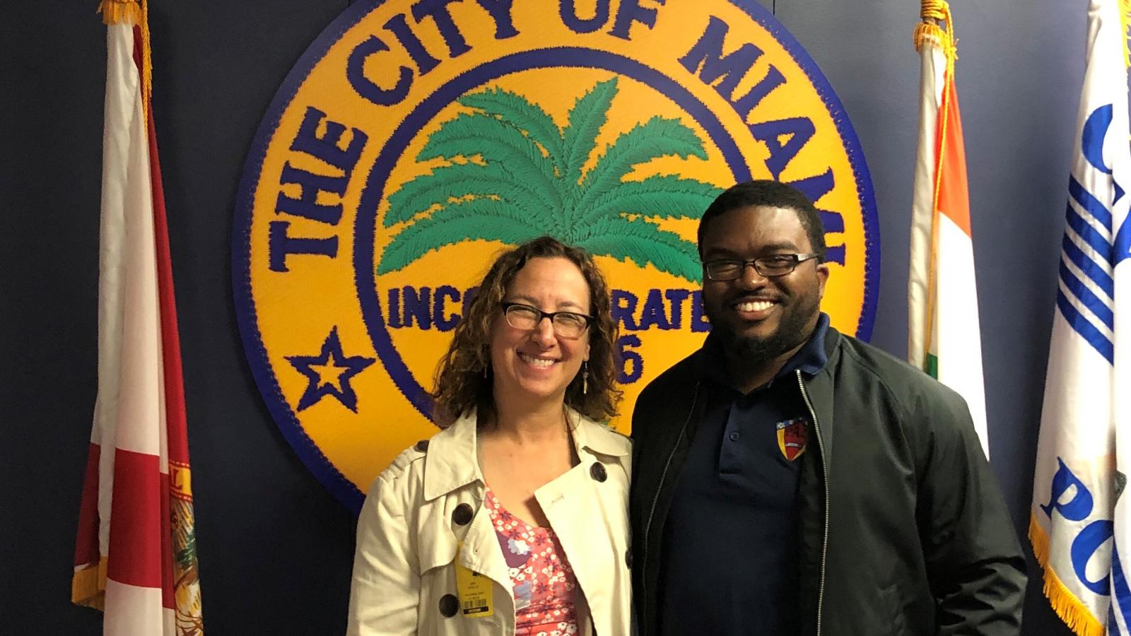 A smiling woman stands with a man in front of a police sign