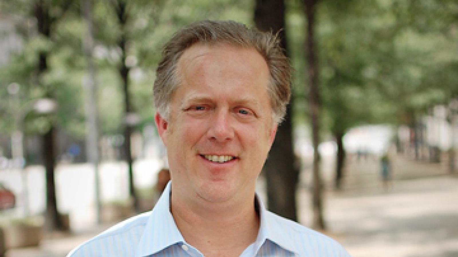 A man in a light blue collared shirt stands outside on a sidewalk