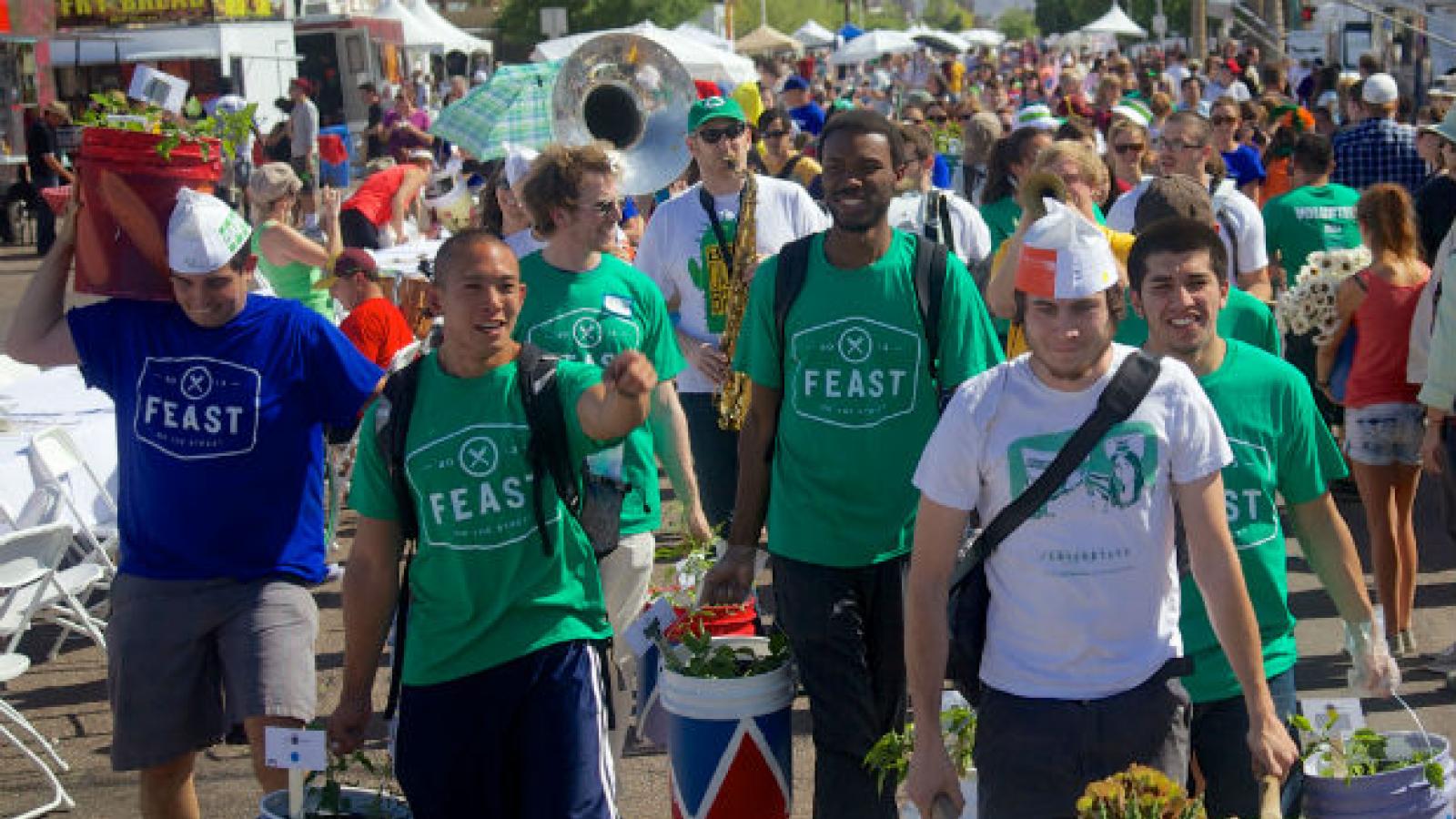 Six young men carry food through a street fair.