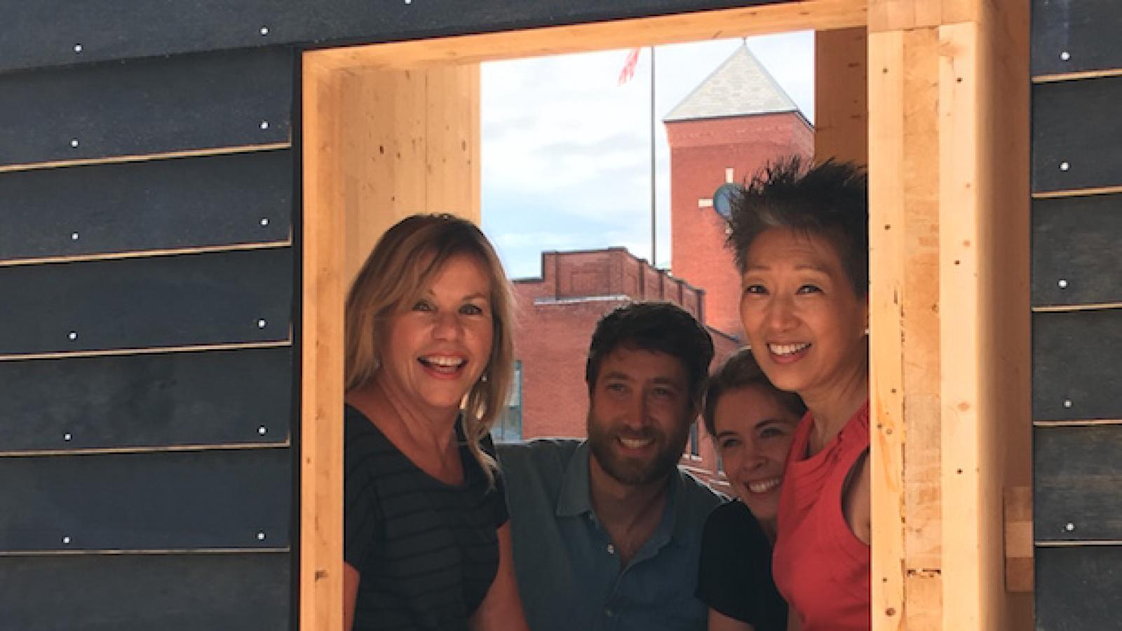 Four people look out the squared window of a small studio space