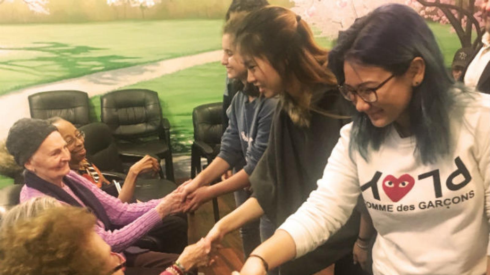 Students participate in Poetry For Life Group of standing teens hold hands with group of seated older adults