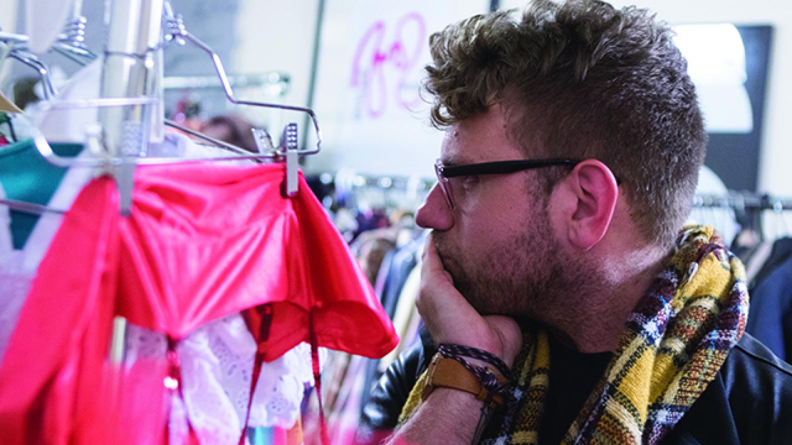 Man in scarf looking at clothes on hangers