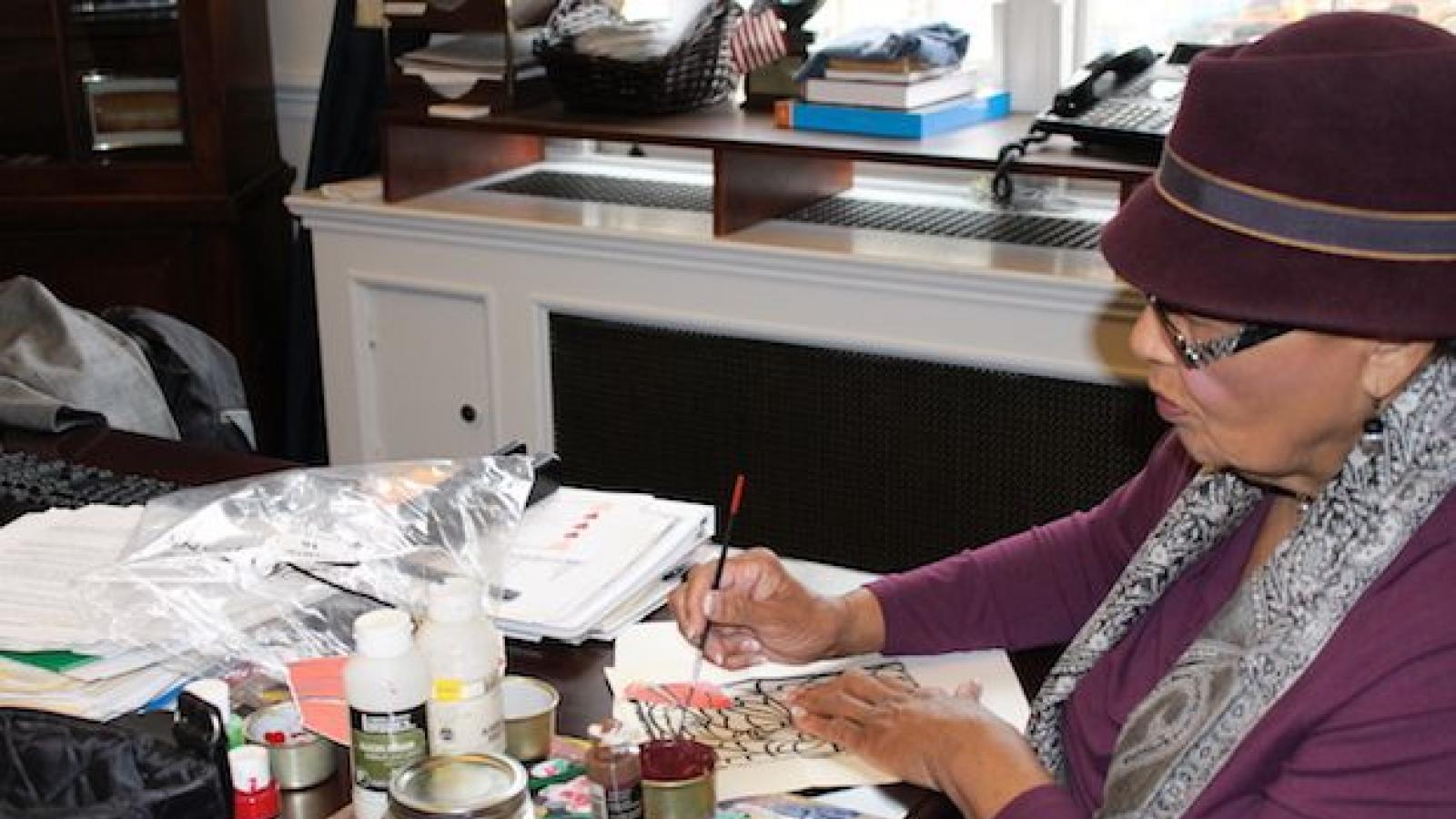 Rep. Adams sitting at her desk painting.