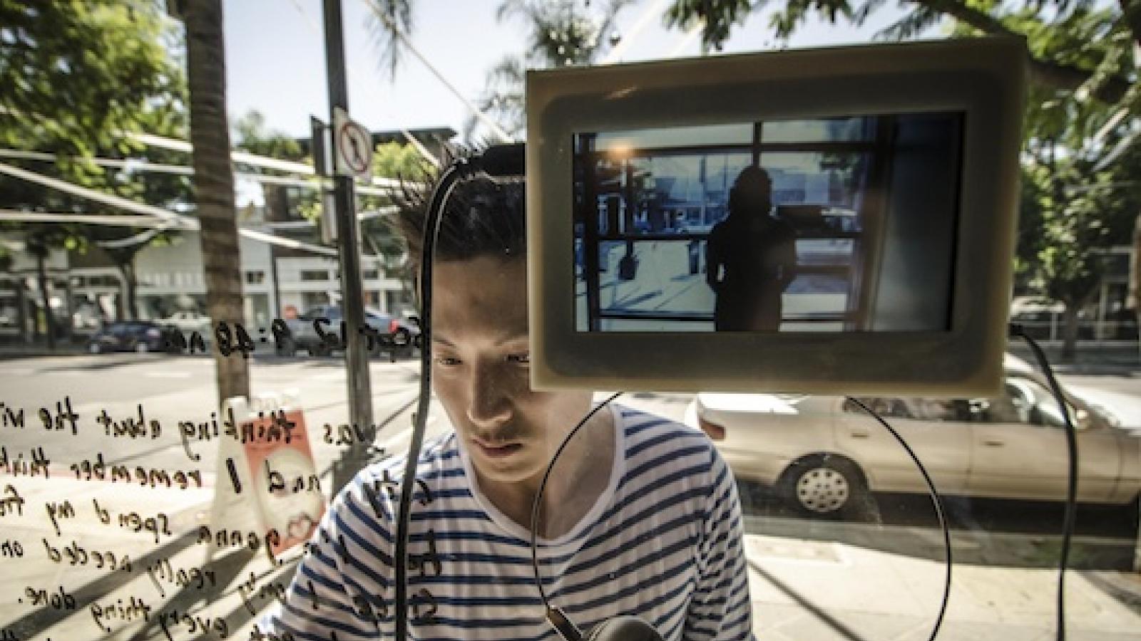 A man interacts with a digital artwork installed in a storefront by writing on glass