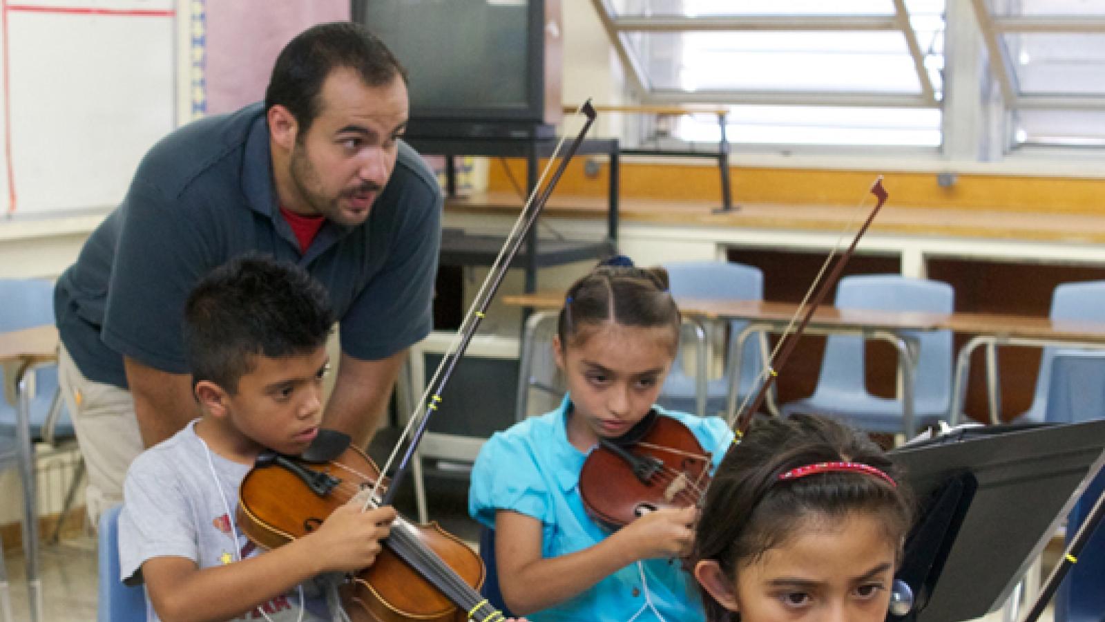 A teaching artist works with three students learning the violin.