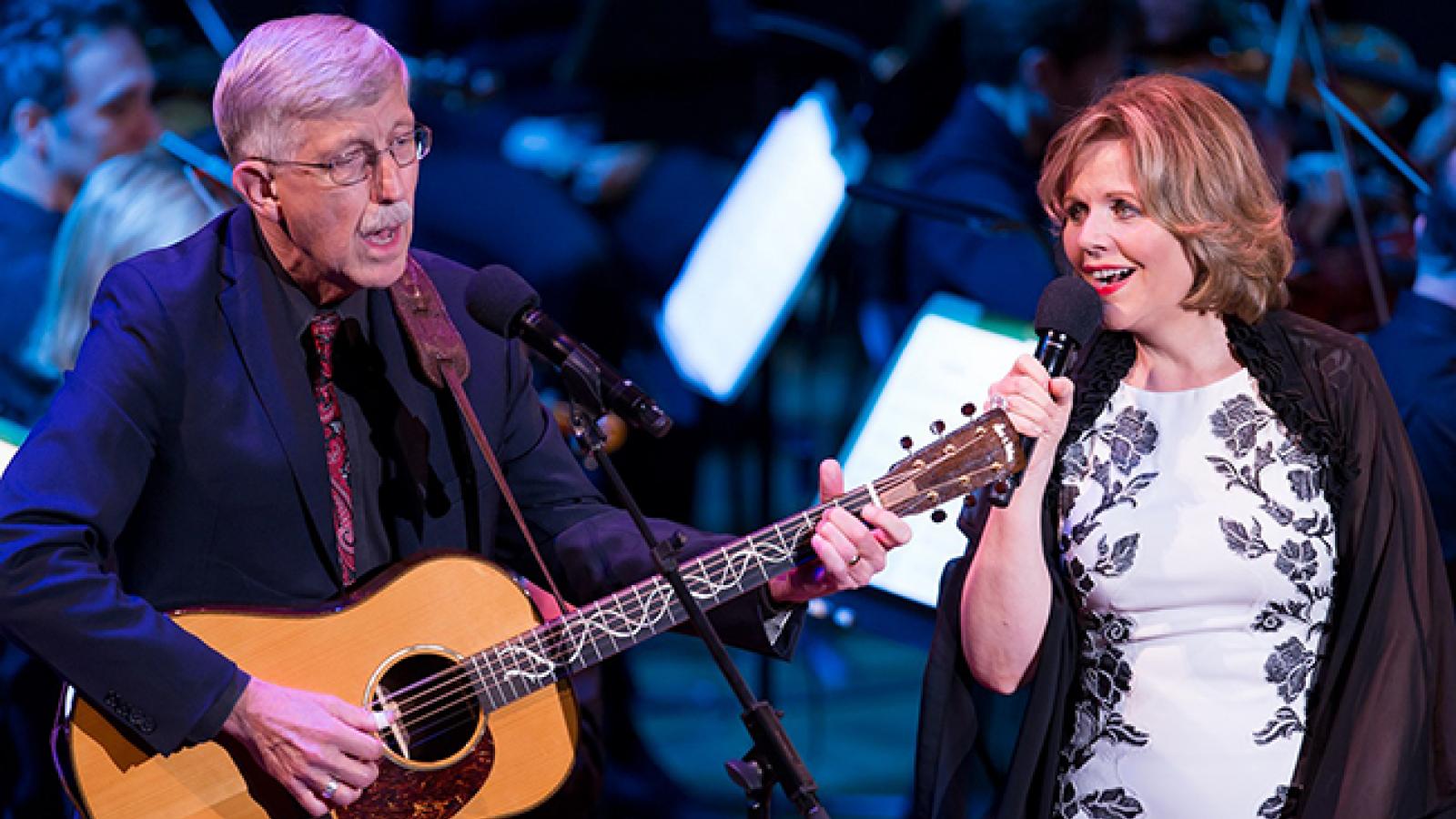 An older man playing a guitar next to a woman singing