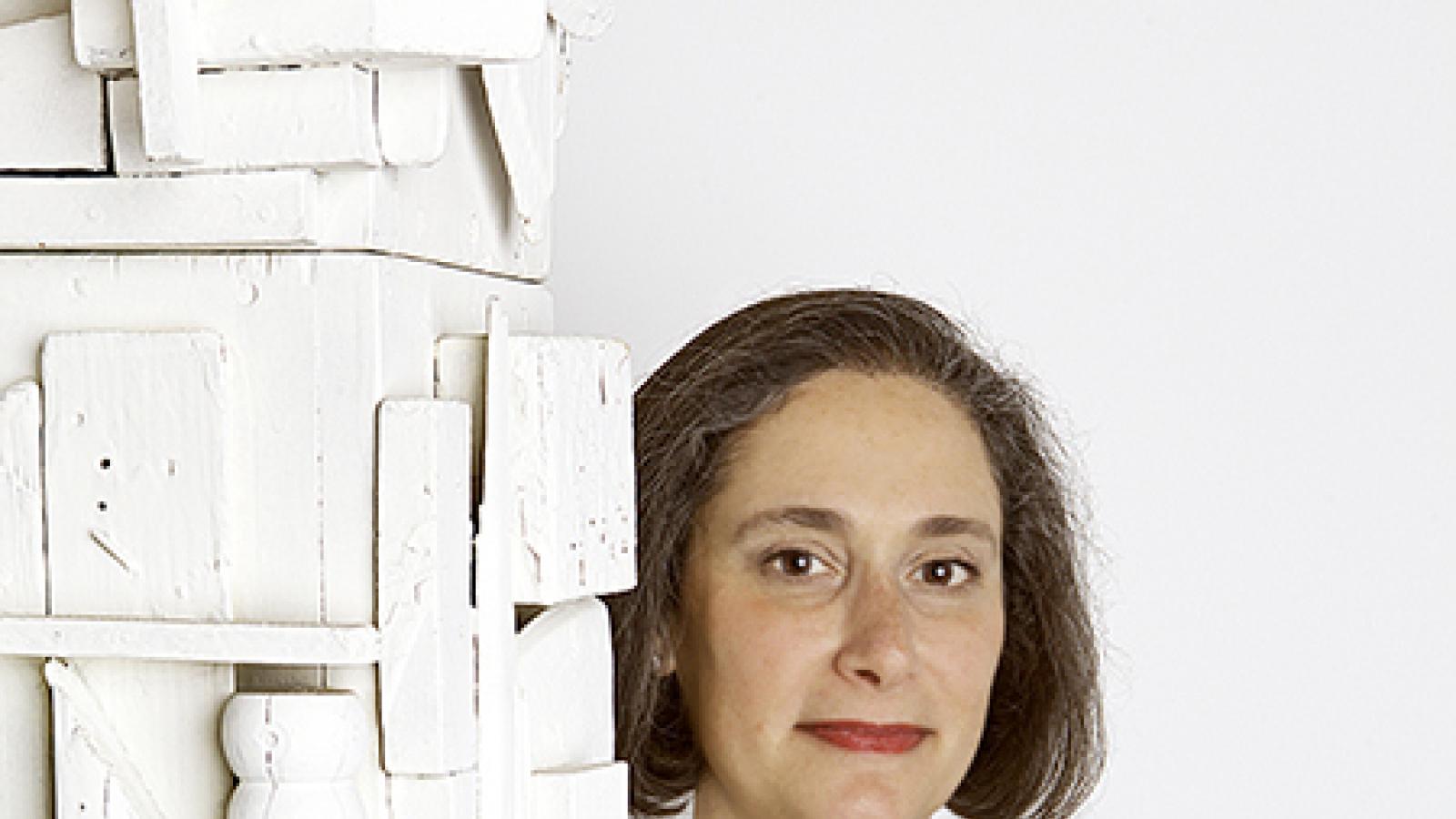 Woman wearing a black suit with large red brooch standing next to a white sculpture.