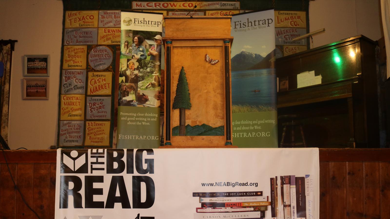 Many colorful posters, a podium, a piano, and a big NEA Big Read banner decorated on a stage.