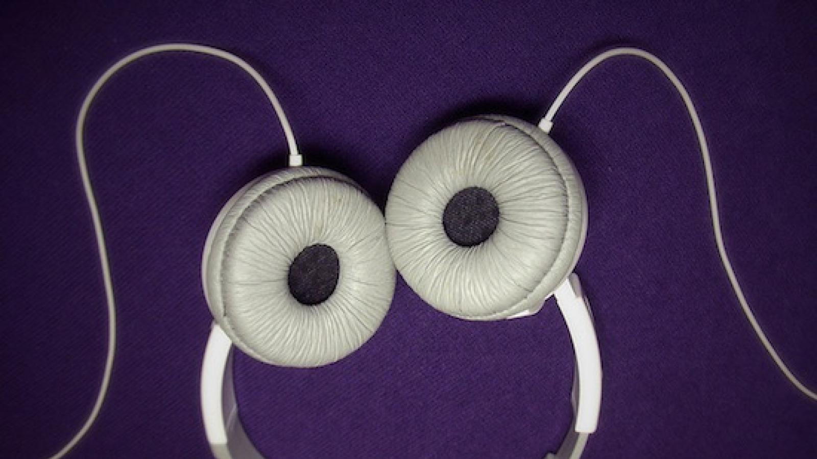 white headphones placed upside down on a purple background so they look like a smily face