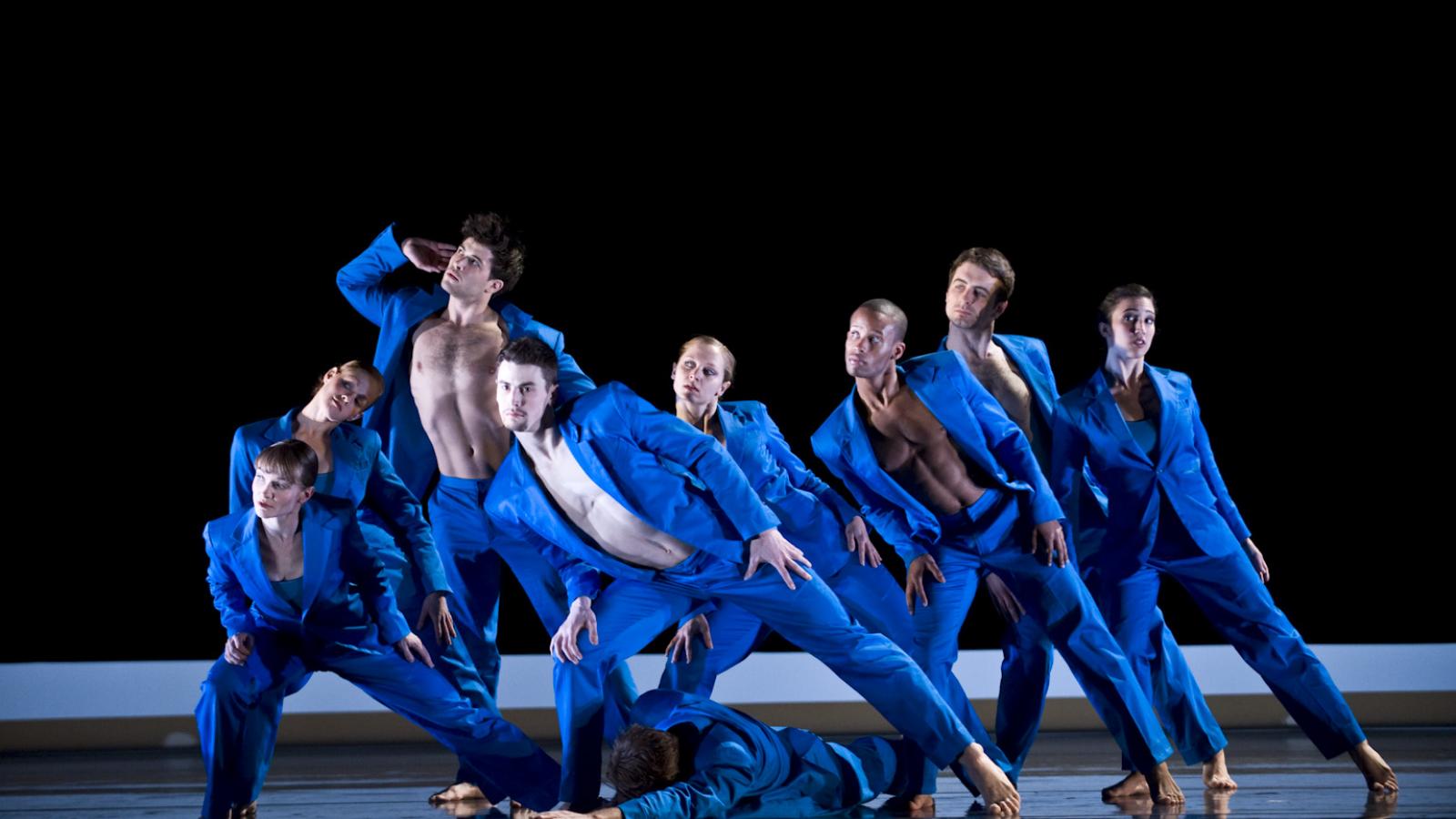 Six dancers dressed in blue on stage.