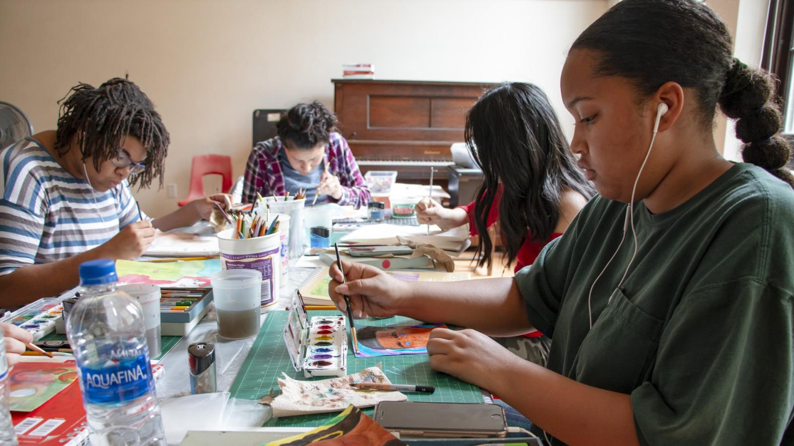 Group of kids sitting at table painting.