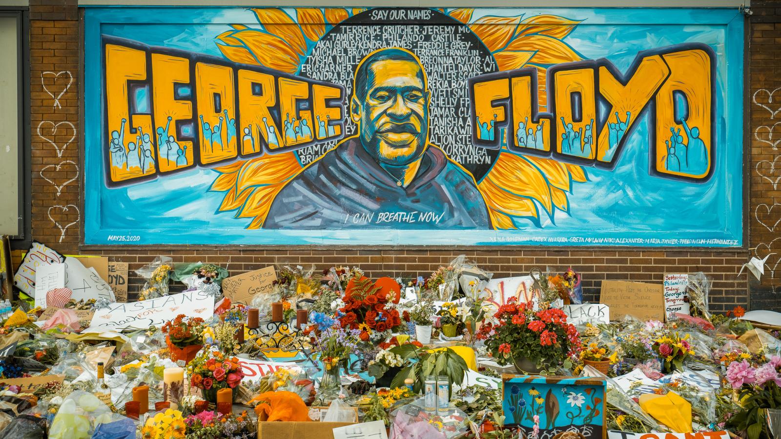 A painting of George Floyd on a building side with flowers in front of it. 