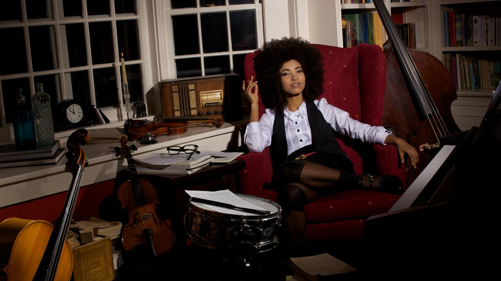 Woman sitting in room surrounded by bass instruments. 