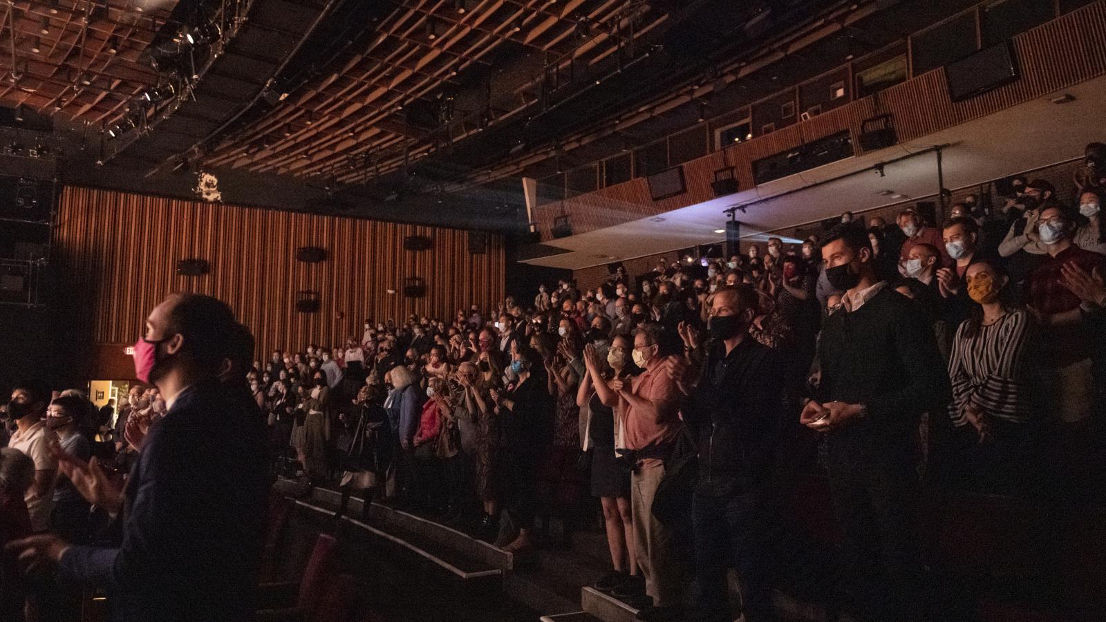 Rows of audience members wearing masks and sitting in a performing arts venue waiting for a performance.