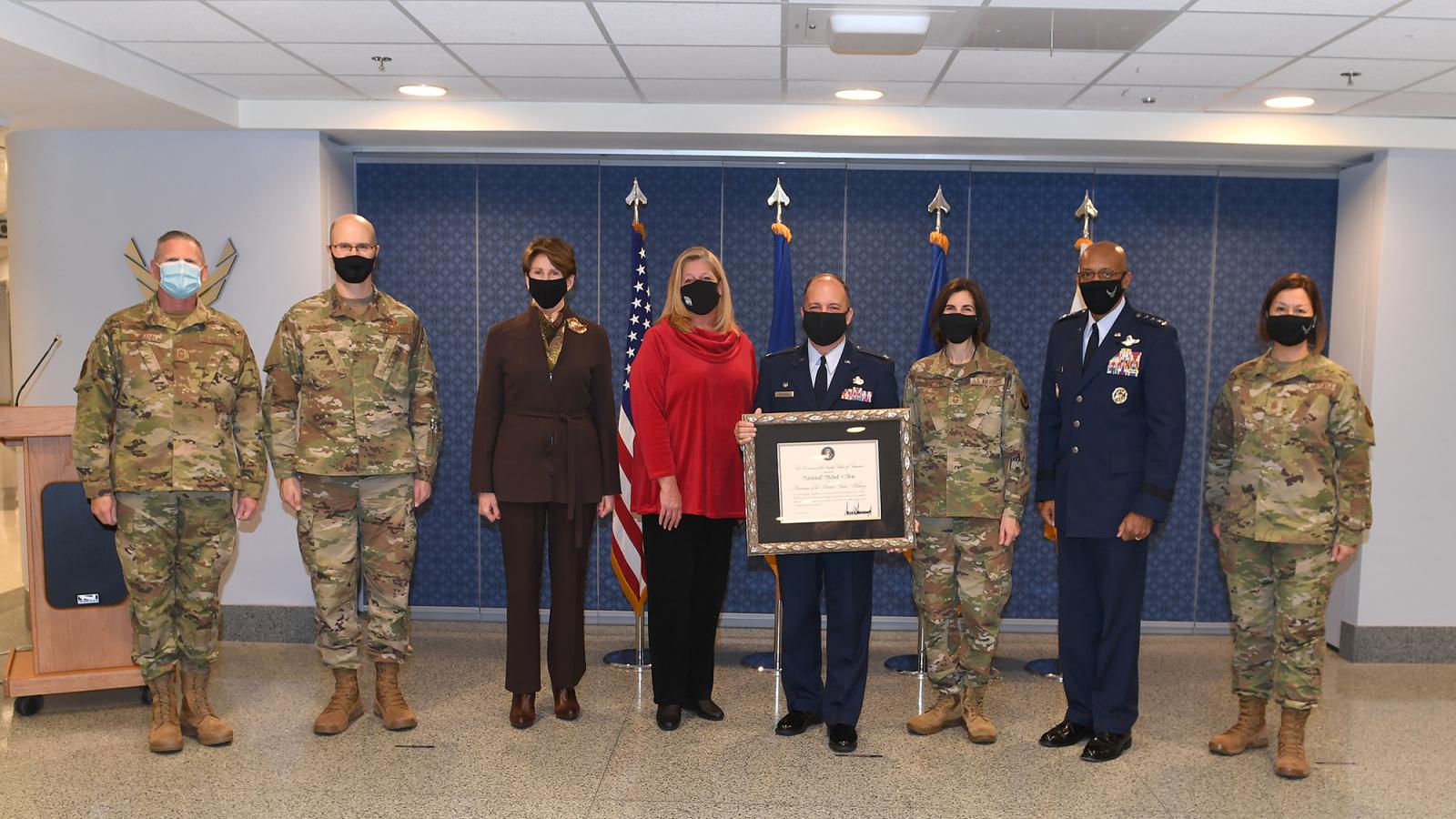 Woman standing with military service members, all wearing masks.