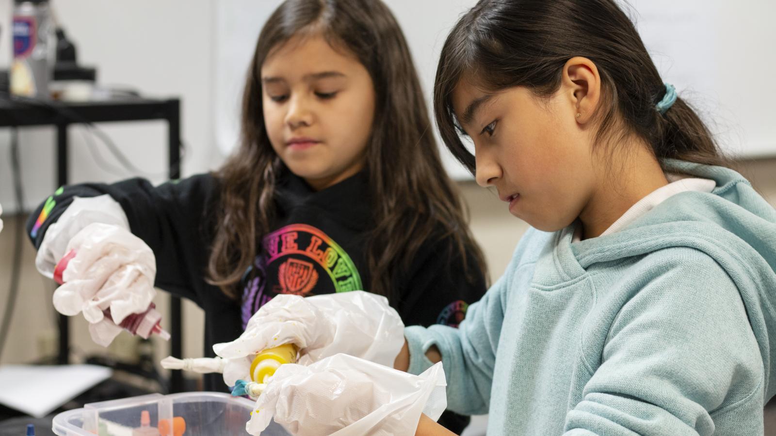 Two girls gluing items during an arts class.